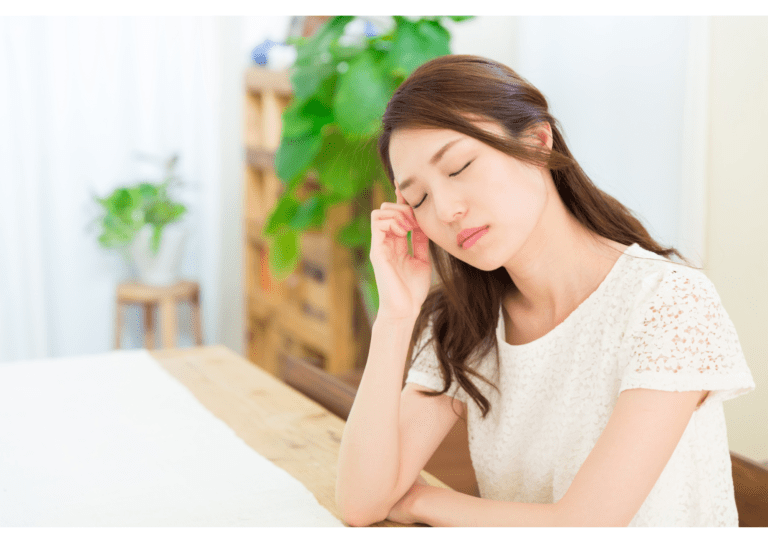 疲れや緊張で目を閉じ、こめかみに手を当てている女性の様子